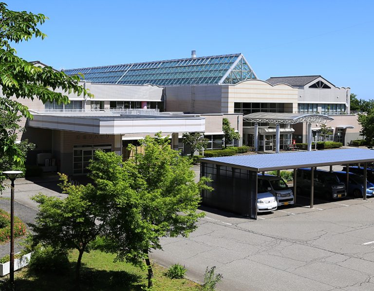 太陽光パネル装備の大型介護施設建物。駐車場・庭園を備えた外観全景。